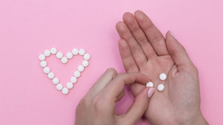 Eine Tablette in einer Hand, daneben ein Herz aus Tabletten