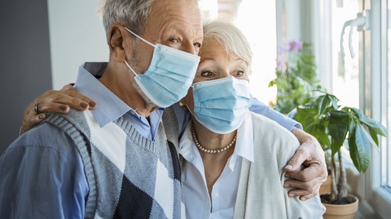 Ein herzkrankes älteres Paar steht mit Mundschutz im Raum, um sich vor Corona zu schützen. 