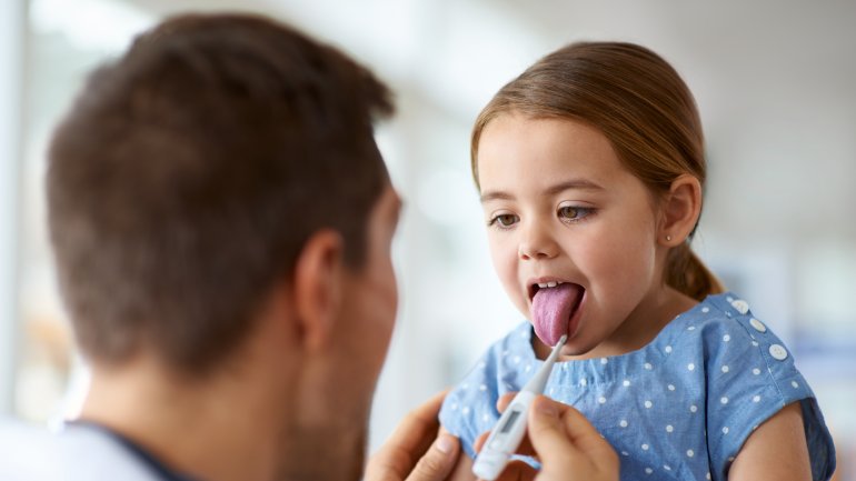  Kawasaki-Syndrom: Arzt untersucht die Zunge und misst Fieber bei betroffenem Mädchen.